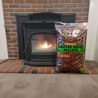 Black pellet stove with a bag of coffee husk pellets in front of a brick wall.