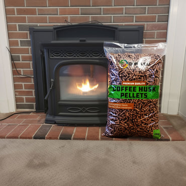 Black pellet stove with a bag of coffee husk pellets in front of a brick wall.